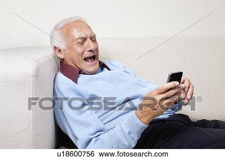 Stock Photograph - Happy elderly man using cell phone at home. Fotosearch