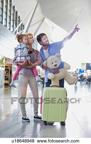 Stock Photo - Happy family on a holiday looking at their flight on monitor in airport with lens flare. Fotosearch