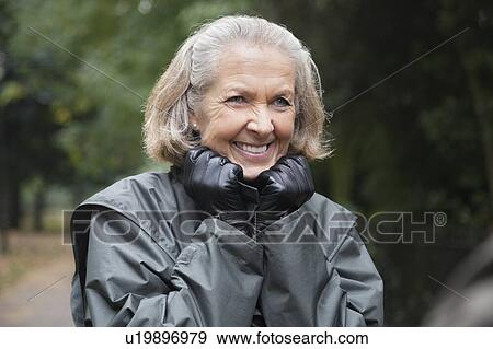 Stock Photo - Happy senior woman in winter coat standing at park. Fotosearch