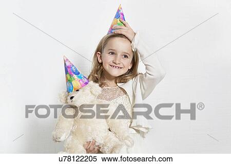 Happy young birthday girl wearing party hat with teddy bear over colored background View Large Photo Image Stock Photography - Happy young birthday girl wearing party hat with teddy bear over colored background. Fotosearch