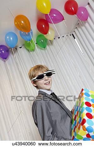 Stock Image - Happy young boy wearing sunglasses holding gift in party. Fotosearch