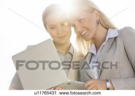 Happy young businesswomen using laptop against sky View Large Photo Image Stock Image - Happy young businesswomen using laptop against sky. Fotosearch