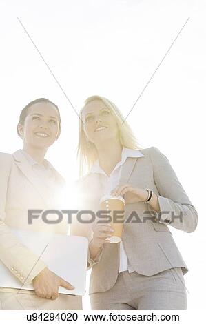 Happy young businesswomen with disposable cup and laptop against sky View Large Photo Image Stock Image - Happy young businesswomen with disposable cup and laptop against sky. Fotosearch