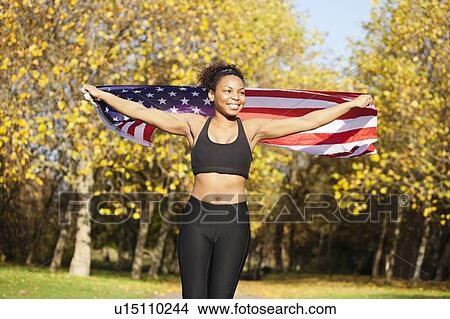 Picture - Happy young female holding up American flag in park. Fotosearch