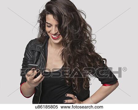 Stock Photography - Happy young female using cell phone against gray background. Fotosearch