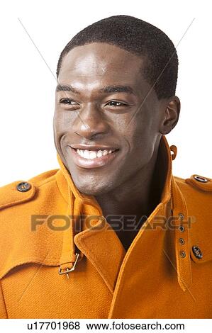Stock Photo - Happy young man in orange trench coat smiling against white background. Fotosearch