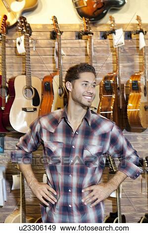 Happy young music store owner with hands on hips standing in front of guitars View Large Photo Image Stock Photo - Happy young music store owner with hands on hips standing in front of guitars. Fotosearch