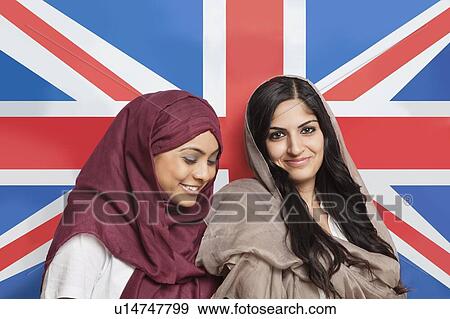 Stock Photo - Happy young Muslim women in traditional clothing standing against British flag. Fotosearch