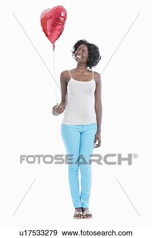 Stock Photo - Happy young woman looking at heart shaped balloon over white background. Fotosearch
