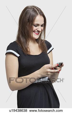 Stock Photo - Happy young woman text messaging through cell phone over gray background. Fotosearch
