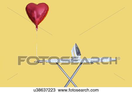 Stock Image - Heart shaped balloon tied to ironing board over yellow background. Fotosearch