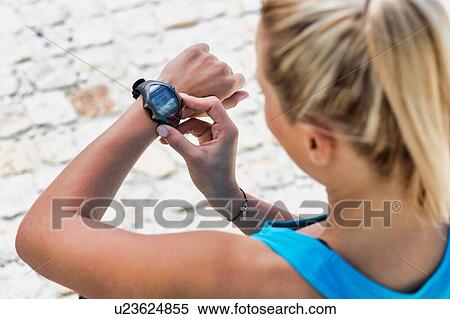 Stock Photography - High angle view of young attractive woman looking at her wristwartch after running in park. Fotosearch