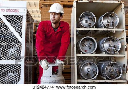 Picture - Hispanic worker inspecting gas canister. Fotosearch