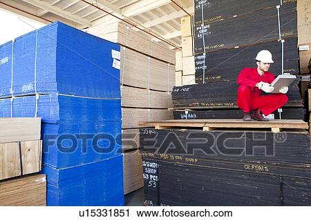 Stock Image - Hispanic worker inspecting tablet PC in timber warehouse. Fotosearch
