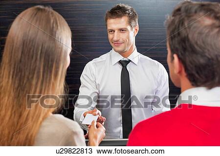 Stock Image - Hotel receptionist giving key card to the guest in lobby. Fotosearch