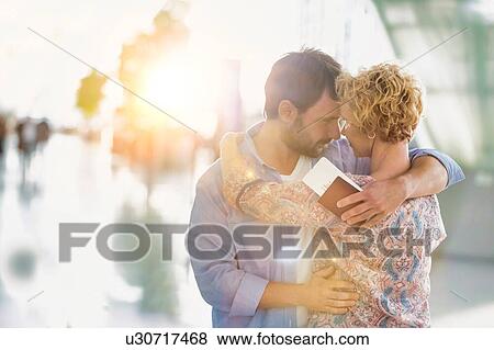 Stock Photo - Husband embracing his wife in airport with lens flare. Fotosearch