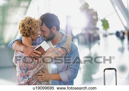 Stock Photography - Husband embracing his wife in airport with lens flare. Fotosearch