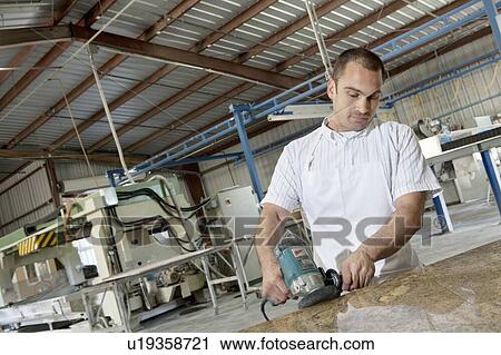 Stock Image - Industrial worker cutting tile with electric saw in factory. Fotosearch