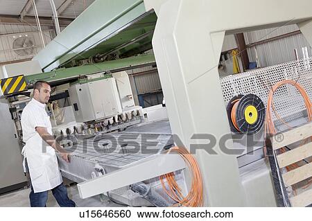 Stock Image - Industrial worker working on machinery in factory. Fotosearch