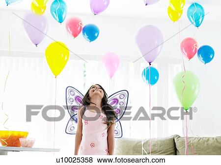 Stock Photo - little girl at her birthday party looking at balloons. Fotosearch