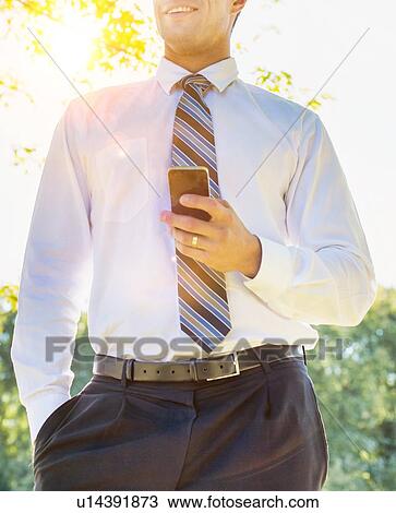 Stock Image - Low angle view of handsome mature businessman using smartphone . Fotosearch