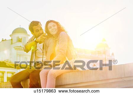 Stock Image - Low angle view of man holding map while sitting and talking to his girlfriend. Fotosearch