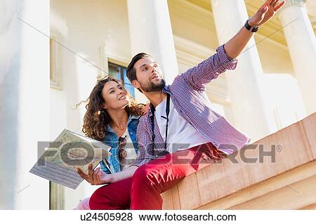 Low angle view of man holding map while sitting and talking to his girlfriend View Large Photo Image Stock Photo - Low angle view of man holding map while sitting and talking to his girlfriend. Fotosearch