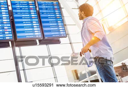 Stock Image - Low angle view of man looking at his flight on screen in airport. Fotosearch