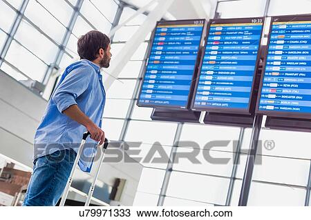 Stock Image - Low angle view of man looking at his flight on screen in airport. Fotosearch
