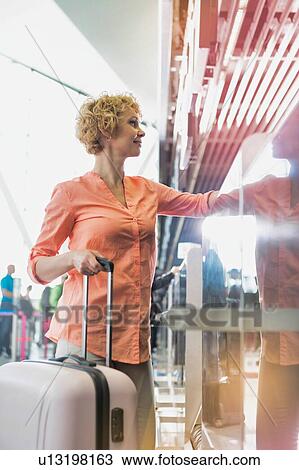 Stock Image - Low angle view of mature woman giving her passport and checking in to get her boarding pass at airport. Fotosearch