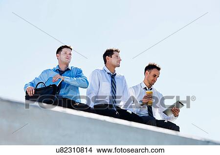 Low angle view of thoughtful mature businessmen sitting and relaxing on rooftop during break in office View Large Photo Image Picture - Low angle view of thoughtful mature businessmen sitting and relaxing on rooftop during break in office. Fotosearch