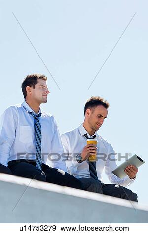 Stock Photo - Low angle view of thoughtful mature businessmen sitting and relaxing on rooftop during break in office. Fotosearch