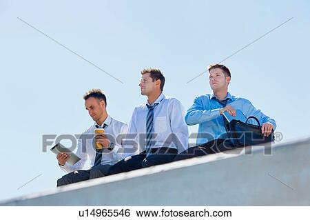 Low angle view of thoughtful mature businessmen sitting and relaxing on rooftop during break in office View Large Photo Image Stock Photograph - Low angle view of thoughtful mature businessmen sitting and relaxing on rooftop during break in office. Fotosearch