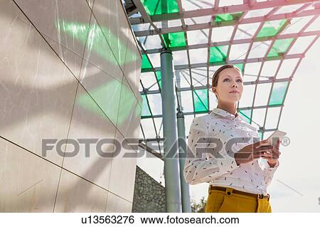 Stock Photograph - Low angle view of young attractive businesswoman standing while using smartphone . Fotosearch