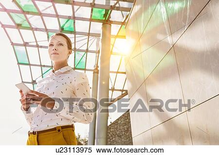 Low angle view of young attractive businesswoman standing while using smartphone View Large Photo Image Stock Photography - Low angle view of young attractive businesswoman standing while using smartphone . Fotosearch