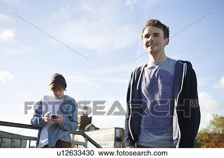 Low angle view of young man using mobile phone with friend in foreground View Large Photo Image Stock Image - Low angle view of young man using mobile phone with friend in foreground. Fotosearch