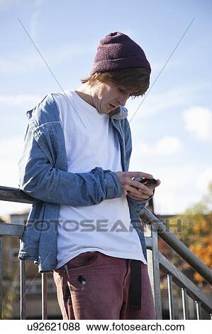 Stock Photo - Low angle view of young man using mobile phone against sky. Fotosearch