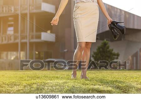 Low section of young businesswoman holding footwear in office lawn View Large Photo Image Stock Image - Low section of young businesswoman holding footwear in office lawn. Fotosearch