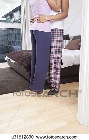 Stock Image - Low section of young couple embracing beside bed. Fotosearch