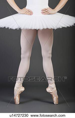 Stock Image - Low section of young female ballet dancer wearing white tutu and ballet slippers. Fotosearch