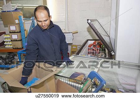 Stock Photo - Male worker loading products in refrigerator at grocery store. Fotosearch