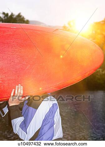 Stock Image - Man carrying kayak outdoors. Fotosearch