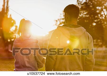 Man embracing her girlfriend after work out in park with lens flare View Large Photo Image Picture - Man embracing her girlfriend after work out in park with lens flare. Fotosearch
