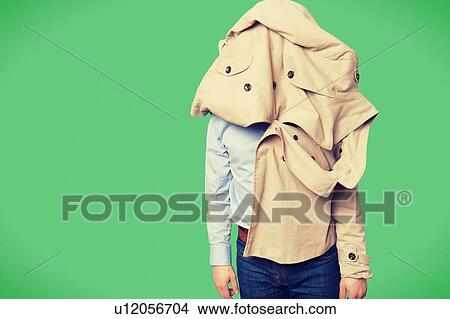 Picture - Man given up on trying to put a coat on as it on his head. Fotosearch
