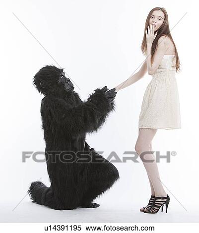 Stock Photography - Man in gorilla costume proposing surprised young woman against white background. Fotosearch