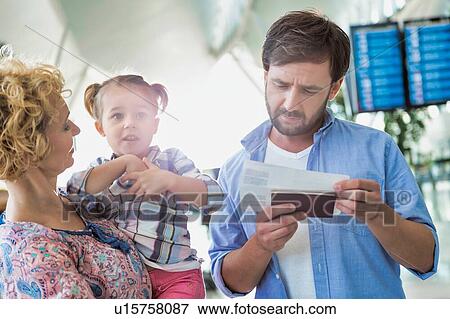 Stock Photo - Man looking on boarding pass while his wife is carrying their daughter in airport. Fotosearch