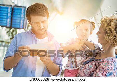 Man looking on boarding pass while his wife is carrying their daughter in airport View Large Photo Image Stock Photo - Man looking on boarding pass while his wife is carrying their daughter in airport. Fotosearch