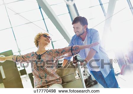 Man pushing baggage cart for check in while his wife is sitting in airport View Large Photo Image Stock Photo - Man pushing baggage cart for check in while his wife is sitting in airport . Fotosearch