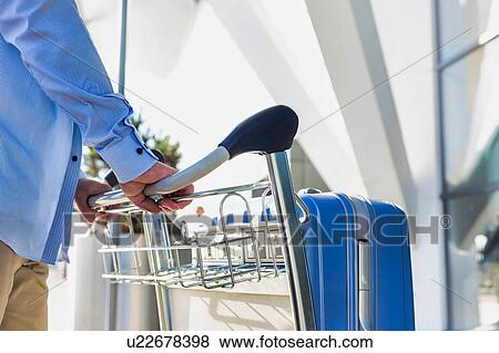 Stock Photo - Man pushing cart with his luggage in airport. Fotosearch