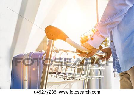 Stock Photograph - Man pushing cart with his luggage in airport. Fotosearch